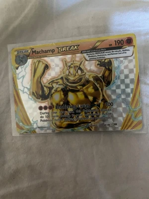 Machamp BREAK Pokémonkort - Machamp BREAK är ett samlarkort från Pokémon TCG med en guldig, holografisk design och coolt rutmönster. Kortet har 190 HP och attacken Boomerang Lariat. Perfekt för dig som gillar att samla eller spela Pokémonkort.
