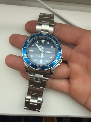 Seiko 5 Sports blå klocka - Snygg Seiko 5 Sports klocka med blå urtavla och blå vridring. Klockan har dag- och datumvisning samt robust armband i silverfärgat rostfritt stål. Perfekt accessoar för dig som gillar stilren och sportig design.