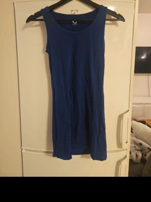 Blått långt linne - En enkel och stilren med rund halsringning och ärmlös design. Linnet har en rak passform och är tillverkad i ett mjukt tyg, perfekt för varma dagar eller som basplagg att styla upp.