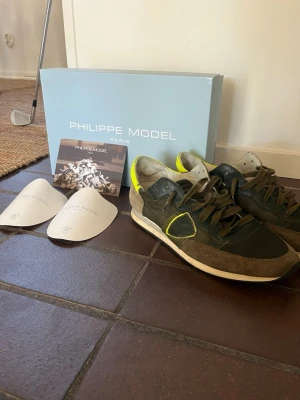 Phillipe model trainers i grön färg  - Snygga sneakers i storlek 41 från Phillipe model, skorna är använda i ca 1 år och är lagade (bild 3) men det är inget som syns. Allt medföljs dvs orginal skolåda, skopapper, pappers skrovliga och lappen med philllipe models logga. Priset är inte hugget i sten skriv vid minsta fundering Med vänlig hälsning, Ville