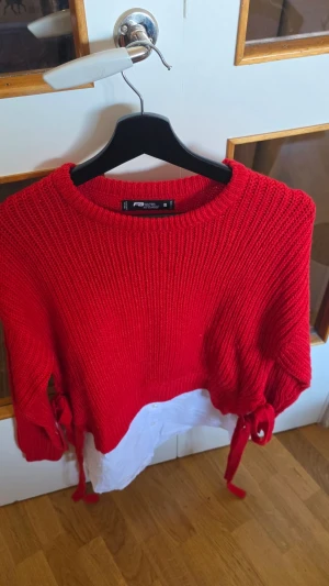 Röd stickad tröja från FB Sister - Snygg röd stickad tröja från FB Sister med rund halsringning och knytband i sidorna. Tröjan har en rak passform och är perfekt för att ge din outfit en färgklick. Mjuk och skön att bära, passar till många olika stilar.