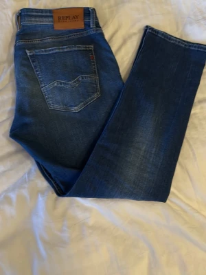 Blå jeans från Replay 33x30 - Snygga blå jeans från Replay med klassisk femficksdesign och läderpatch med logga bak i midjan. Jeansen har raka ben och är tillverkade i ett mjukt denimtyg med lätt tvättad look. Perfekta för dig som gillar stilrena och tidlösa jeans.