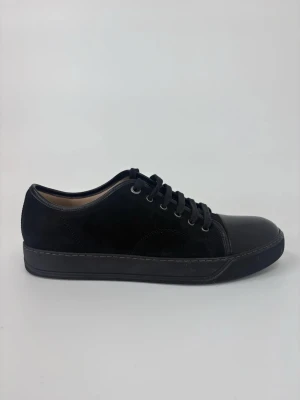Svarta Lanvin sneakers med läderdetaljer - Stilrena svarta sneakers med ovandel i mocka och blanka läderdetaljer på tån och runt snörningen. Klassisk låg modell med svarta skosnören och sula i gummi. Perfekta för en clean och modern look.