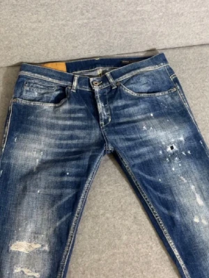 Dondup George Jeans - Säljer ett par blå jeans med slitningar, blekta partier och coola färgstänk. Jeansen har klassisk femficksdesign och smal passform. Snygga kontrastsömmar och råa detaljer ger en trendig look. Perfekta för dig som gillar streetstyle.