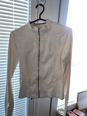 Vit jacka med dragkedja från Gina Tricot - Snygg vit jacka från Gina Tricot med lång ärm och hel dragkedja framtill. Jackan har en stilren design med markerade sömmar och hög krage. Perfekt för dig som gillar en clean och enkel look.