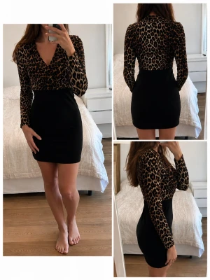 Leopardmönstrad omlottklänning - Snygg kort klänning med leopardmönstrad överdel och svart kjoldel. Omlott-skärning upptill och långa ärmar. Perfekt för dig som vill sticka ut med ett djurmönster och gillar trendiga detaljer.