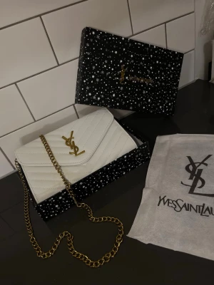Dam väska - En riktig fin vit och guldig YSL väska som är perfekt för dig som vill ha något som känns lyxigt men ändå funkar till allt, både vardag och fest. En sån väska som gör att hela looken känns mer genomtänkt. Allt på bilden följs med. Fraktas inom 24 timmar