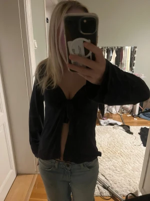 Mörkblå långärmad bolerotopp med knyt - Säljer en mörkblå långärmad bolerotopp med knyt framtill. Toppen har en djup v-ringning och är croppad, vilket ger en trendig look. Perfekt att styla med jeans eller kjol för en cool outfit.