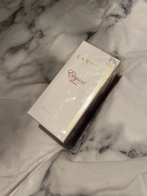 La Rive Elegant Woman Eau de Parfum - La Rive Elegant Woman Eau de Parfum i en stilren, ljusbeige kartong med gulddetaljer och elegant design. Flaskan rymmer 100 ml och doften är inspirerad av fransk parfymkonst. Perfekt för dig som gillar klassiska och feminina dofter.