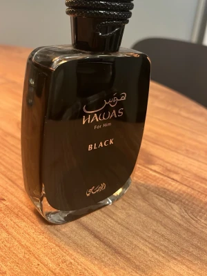 Hawas For Him Black parfym - Snygg parfymflaska i svart glas från Hawas, modellen For Him Black. Flaskan har en elegant, fyrkantig form med guldfärgad text och detaljer. Perfekt för dig som gillar stilrena och maskulina dofter.