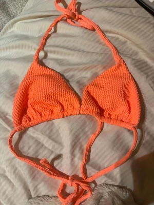 Orange trekantsbikini med knyt - Säljer en snygg orange trekantsbikini med ribbad struktur. Bikinin har knyt både i nacken och ryggen för justerbar passform. Perfekt för sommaren och strandhäng! Helt oanvänd men den är dock från SHEIN, men i helt perfekt kvalité.