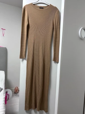 Beige ribbad långklänning - Säljer en beige ribbad långklänning med lång ärm och rund halsringning. Klänningen är figurnära och gjord i ett stretchigt stickat material som sitter snyggt på kroppen. Perfekt för en stilren och enkel look.