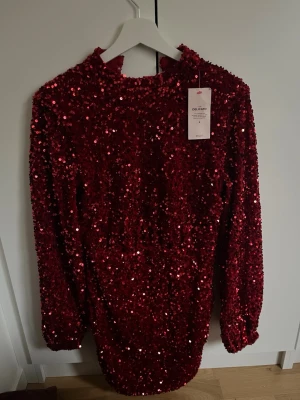Röd paljettklänning med öppen rygg - Säljer en glittrig röd paljettklänning från Delicatel. Klänningen har lång ärm, kort längd och en snygg öppen rygg. Perfekt för dig som vill sticka ut med en statement piece. Materialet är polyester och paljetterna ger ett riktigt partyvibe.