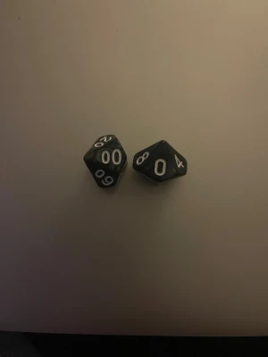 Svarta tiosidiga rollspelstärningar - Två svarta tiosidiga tärningar med vita siffror, perfekta för rollspel som Dungeons & Dragons eller andra brädspel. Tillverkade i plast och har tydliga siffror för enkel avläsning.