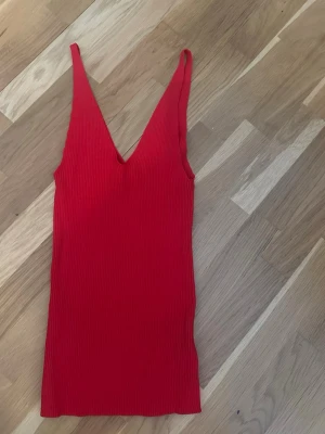 Ribbad röd linnetopp med v-ringning - Snygg ribbad röd linnetopp med djup v-ringning och smala axelband. Perfekt för dig som gillar en enkel. Materialet är mjukt och stretchigt, vilket gör den bekväm att bära hela dan.