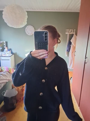 Svart ribbstickad kofta💕 - Mysig svart ribbstickad kofta med stora dekorativa knappar framtill och v-ringad hals. Koftan har långa ärmar och en avslappnad passform, perfekt att slänga på sig när det är lite kyligt.💕