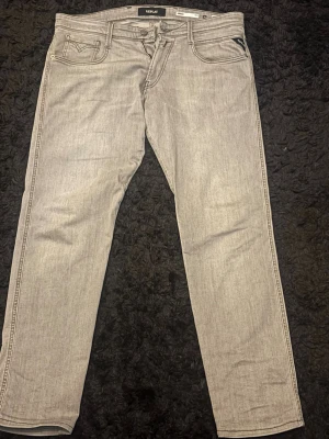 Ljusgrå jeans från Replay - Snygga ljusgrå jeans från Replay med klassisk femficksdesign och raka ben. Jeansen har diskreta sömmar och detaljer på bakfickorna. Perfekta för dig som gillar en stilren och modern look. Modell Anbass