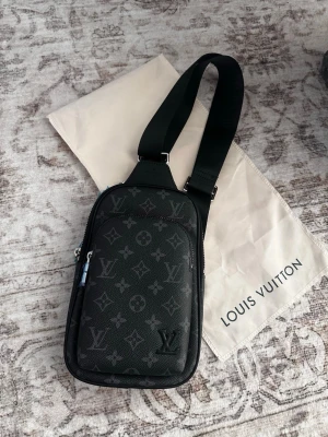 Louis Vuitton svart monogram rygg/axelväska  - Snygg svart rygg/axelväska från Louis Vuitton med klassiskt monogrammönster i grått. Väskan har justerbar axelrem, flera fack med dragkedja och är tillverkad i tåligt läder. Perfekt för dig som vill ha en stilren och exklusiv accessoar.