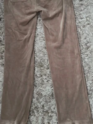 Beiga mjukisbyxor i velour Juicy Couture - Säljer ett par beiga mjukisbyxor i velour från Juicy Couture. Byxorna har raka ben, stora fickor fram och en broderad JC-logga på ena fickan. Perfekta för en avslappnad och trendig look! Kommer ej till användning:)