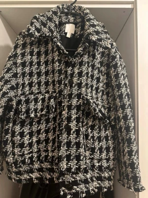 Svartvit rutig cardiganjacka - Säljer en svartvit rutig cardiganjacka med grov stickad känsla och stora knappar framtill. Jackan har bred krage, två fickor på bröstet och en boxig passform. Perfekt för dig som gillar statement-plagg och vill sticka ut lite extra.