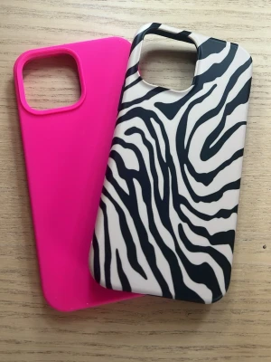 Två mobilskal, zebra och rosa (iPhone 13 Pro Max) - Säljer två snygga mobilskal. Ett är helrosa i mjukt silikonmaterial och det andra har ett zebramönster i svart och vitt, också i silikon. Båda har öppning för kamera och passar till en modern smartphone. Perfekt för dig som vill variera stilen på mobilen.
