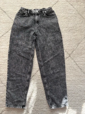 Svarta  jeans med tvättad look - Säljer ett par svarta jeans med snygg tvättad effekt och hög midja. Jeansen har raka ben, klassiska fem fickor och bälteshällor. Stängs med knapp och dragkedja. Perfekta för en avslappnad och trendig stil. Använda ett fåtalgånger och mycket bra kvalitet!