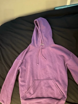 Lila Bikbok hoodie med ficka och huva - Lila hoodie med stor ficka på magen och justerbar huva med snören. Klassisk modell med ribbade muddar vid ärmslut och nederkant. 