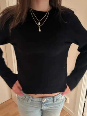 Svart croppad stickad tröja - En enkel svart stickad tröja med croppad passform och långa ärmar. Tröjan har rund halsringning och är gjord i ett mjukt material som passar perfekt till jeans eller kjol. Stilren och lätt att matcha med olika outfits.