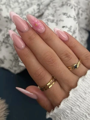 Handgjorda lösnaglar💞 - Säljer ett set långa press-on naglar i ljusrosa med glansig finish. Naglarna har en spetsig almondform och dekoreras med vitt vågmönster samt en liten blomdetalj på en nagel.