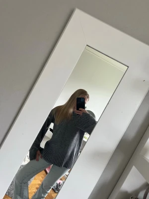 Grå oversized stickad tröja - Mysig grå stickad tröja med oversized passform och breda ribbade muddar vid ärmslut och nederkant. Tröjan har en enkel design utan synligt märke och är perfekt för lager på lager. Materialet känns mjukt och värmande.