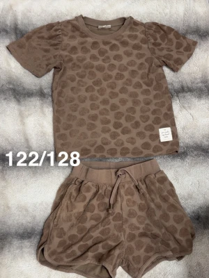 Brunt set med prickar från pompdelux - Säljer ett brunt tvådelat set från pompdelux med kortärmad t-shirt och shorts. Båda delarna har ett prickigt mönster. Shortsen har dragsko i midjan 🌸 Fint använt skick. Storlek 122/128