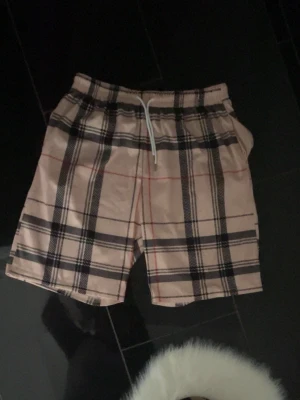 Beige rutiga shorts med snörning - Snygga beige shorts med klassiskt rutigt mönster och snörning i midjan. Perfekta för sommardagar och har en avslappnad passform. Stilen är inspirerad av streetwear och passar dig som gillar trendiga plagg.