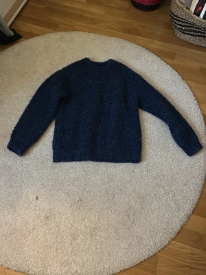 Mörkblå stickad tröja från Zara - Mysig mörkblå stickad tröja från Zara med grov struktur och rund halsringning. Tröjan har långa ärmar och är tillverkad i ett fluffigt material som känns riktigt skönt. Perfekt för dig som gillar en enkel och stilren look.