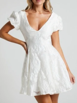 Vit kort klänning från Showpo - Supersöt vit kort klänning med puffärmar och v-ringning. Klänningen har ett subtilt blommigt mönster i tyget och markerad midja som ger en feminin siluett. Perfekt för studenten!