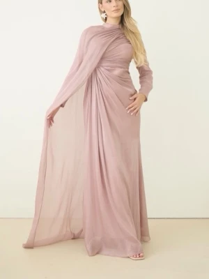 Lång rosa draperad klänning - Elegant långklänning i ljusrosa med draperad design och ett svepande, transparent tyg över ena axeln. Klänningen har en asymmetrisk form och är gjord i ett lätt, flödande material som ger ett exklusivt intryck. Perfekt för dig som vill sticka ut med en unik look. Aldrig använt 
