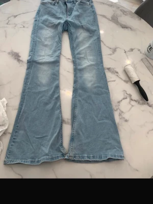 Ljusblå utsvängda jeans - Säljer ett par ljusblå jeans med utsvängda ben och klassisk femficksmodell. Jeansen har en snygg tvätt med lätt slitning på låren och är perfekta för dig som gillar retrostil och vill sticka ut. Materialet är denim i bomull.