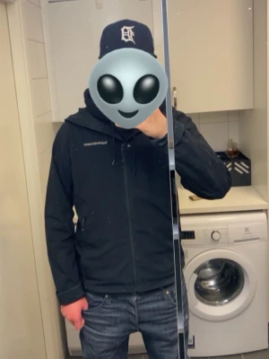 Svart vindjacka från Peak Performance - Snygg svart vindjacka från Peak Performance med huva och dragkedja framtill. Jackan har en minimalistisk design med diskret logga på bröstet och praktiska fickor. Perfekt för dig som vill ha en stilren och funktionell jacka till vardags. Nypris 2200 kr.