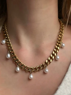 Guldfärgat 9mm bred 18k halsband med pärlor - Snyggt guldfärgat halsband med chunky kedja och vita pärlor som hänger längs kedjan. Halsbandet har en modern och trendig design som passar perfekt för att lyfta din outfit. Materialet är metall och pärlor, och det är ett statement-piece för dig som gillar att sticka ut.