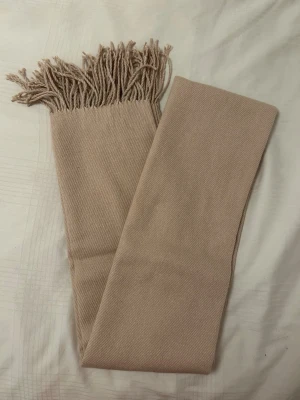 Beige/ros halsduk med fransar från Åhléns - En beige/ros halsduk från Åhléns i mjuk 100% akryl. Halsduken har klassisk design med fransar i ändarna. Aldrig använd. 