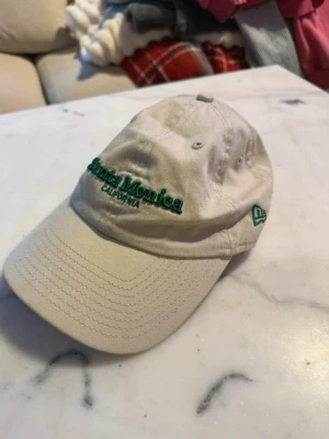 Beige keps från New Era - Säljer en stilren beige keps från New Era, tillverkad i 100% bomull. Klassisk form med böjd skärm och justerbar passform. Perfekt för dig som vill ha en enkel och snygg accessoar till din outfit.