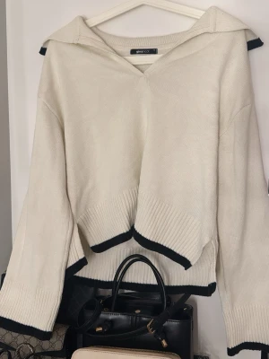 Vit stickad tröja med svarta detaljer - Säljer en vit stickad tröja från Ginatricot med bred krage och svarta kontrastkanter på ärmslut. Tröjan har ett tjockt och mjukt material och sitter otroligt fint på kroppen. Den är köpt för 499kr och är nästan helt oanvänd, utan några skador eller fläckar, den är inte knopprig heller💕