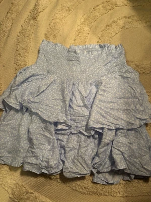 Ljusblå volangkjol från Samsa Collection - Supersöt ljusblå och ljusgrön kortkjol från Samsa Collection med små vita blommor och flera volanger. Kjolen har smock i midjan för en bekväm passform och är perfekt för vår och sommar. Lätt och luftig känsla, passar till många olika stilar. Ljusblå storlek M och ljusgrön storlek S. Man får båda kjolarna för 60 kr. 