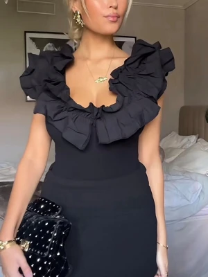 Svart volangklänning med djup urringning - Supersnygg svart body med stora volangdetaljer runt den djupa urringningen. Bodyn är ärmlös och har en figurnära passform som framhäver siluetten. Perfekt för dig som vill sticka ut med en trendig och elegant look.