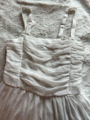 Vit omlottklänning med volang - Säljer en vit klänning med breda axelband och omlottdetaljer. Klänningen har ett vackert volangfall och ett skirt, lätt tyg som ger en romantisk känsla. Perfekt för sommarens alla tillfällen! Helt ny aldrig använt!