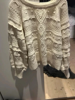Vit stickad tröja med strukturmönster - Säljer en krämvit stickad tröja med snygga strukturmönster och puffiga ärmar. Tröjan har bred ribbad mudd i nederkant och vid ärmslut, samt rund halsringning. Perfekt för dig som gillar en trendig och mysig look.