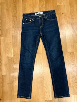 Mörkblå slim jeans från Levi's - Snygga mörkblå jeans från Levi's i modellen slim taper. Klassisk femficksdesign, kontrastsömmar och knappgylf. Perfekta för dig som gillar en smalare passform och tidlös stil. Levi's-logga på insidan av linningen. Helt helt nya aldrig använt, (endast provade) köptes för 550 säljer för 400 hann klippa av lapparna innan jag bestämt mig för att behålla eller inte dom var lite för små !