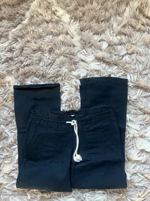 Svarta linnebyxor från Roxy - Snygga svarta linnebyxor från Roxy med avslappnad passform och dragsko i midjan. Byxorna har två framfickor och ett mjukt, luftigt material som passar perfekt till sommaren. Styla med en crop top eller hoodie för en chill look.