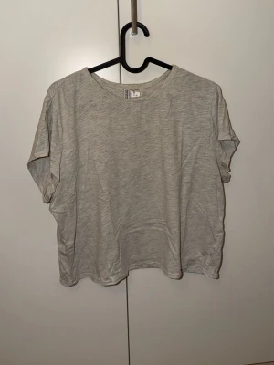 Ljusgrå loose t-shirt från H&M Divided - En enkel och stilren ljusgrå t-shirt från H&M Divided Basic. Modellen är loose fit med korta ärmar och rund halsringning. Perfekt för en avslappnad och bekväm stil. Tillverkad i mjuk bomull som känns skön mot huden.