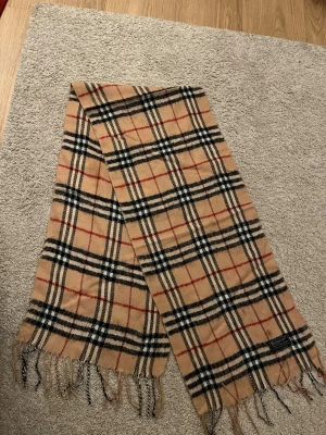Burberry scarf - Jag säljer en modern aprikosfärgad burberry scarf till ett väldigt bra pris med tanke på att den är helt i nyskick. Väldigt snygg och passar till många fina outfits!