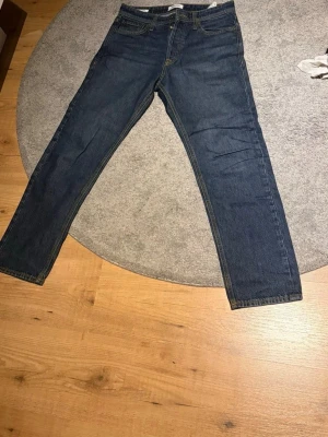 Mörkblå Jack & Jones  - Säljer ett par klassiska mörkblå jeans med rak passform och fem fickor. Jeansen har kontrastsömmar och är tillverkade i denim. Perfekta för en avslappnad och tidlös stil. 